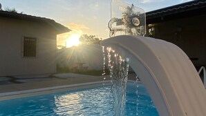 A swimming pool with a water feature, a clear sky, and a building in the background. - House on the River (Barra do Jacuipe)