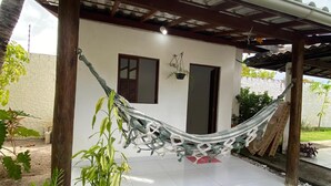 A covered patio area with a hammock, potted plants, and a tiled floor. - House on the River (Barra do Jacuipe)