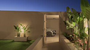 Una casa moderna amb un cotxe a l'interior, una porta que condueix a un garatge i un jardí ben cuidat amb plantes grans.