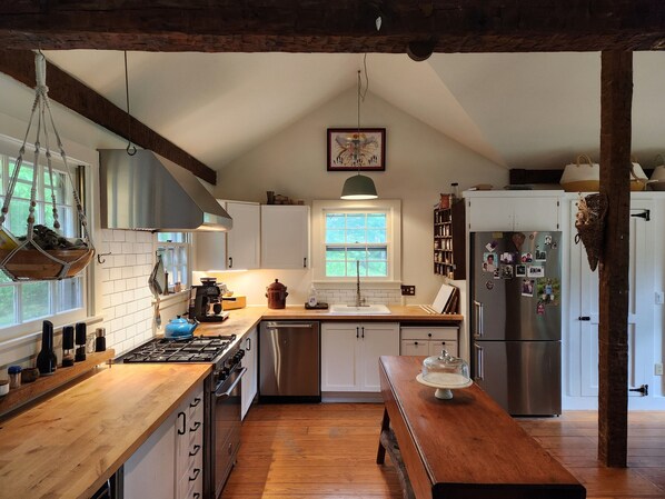 A kitchen with wooden countertops, a hanging pot rack, a stove, a sink, and a refrigerator.