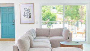 A large L-shaped sectional sofa in a bright room with a large window, a framed abstract artwork, and a teal door.