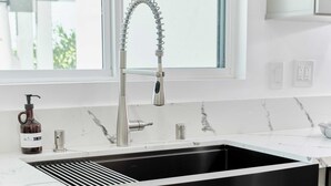 A modern kitchen with a stainless steel sink, a window above the sink, and a bottle of hand soap on the counter.