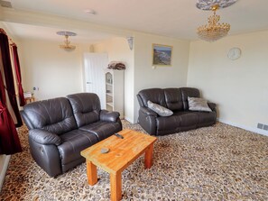 Ein Wohnzimmer mit zwei Ledersofas, einem Holztisch, einer Chandelier, einer Uhr und einem gerahmten Bild an der Wand.