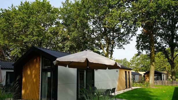 Una zona d'estar exterior moderna amb taula i cadires, envoltada de vegetació i arbres.