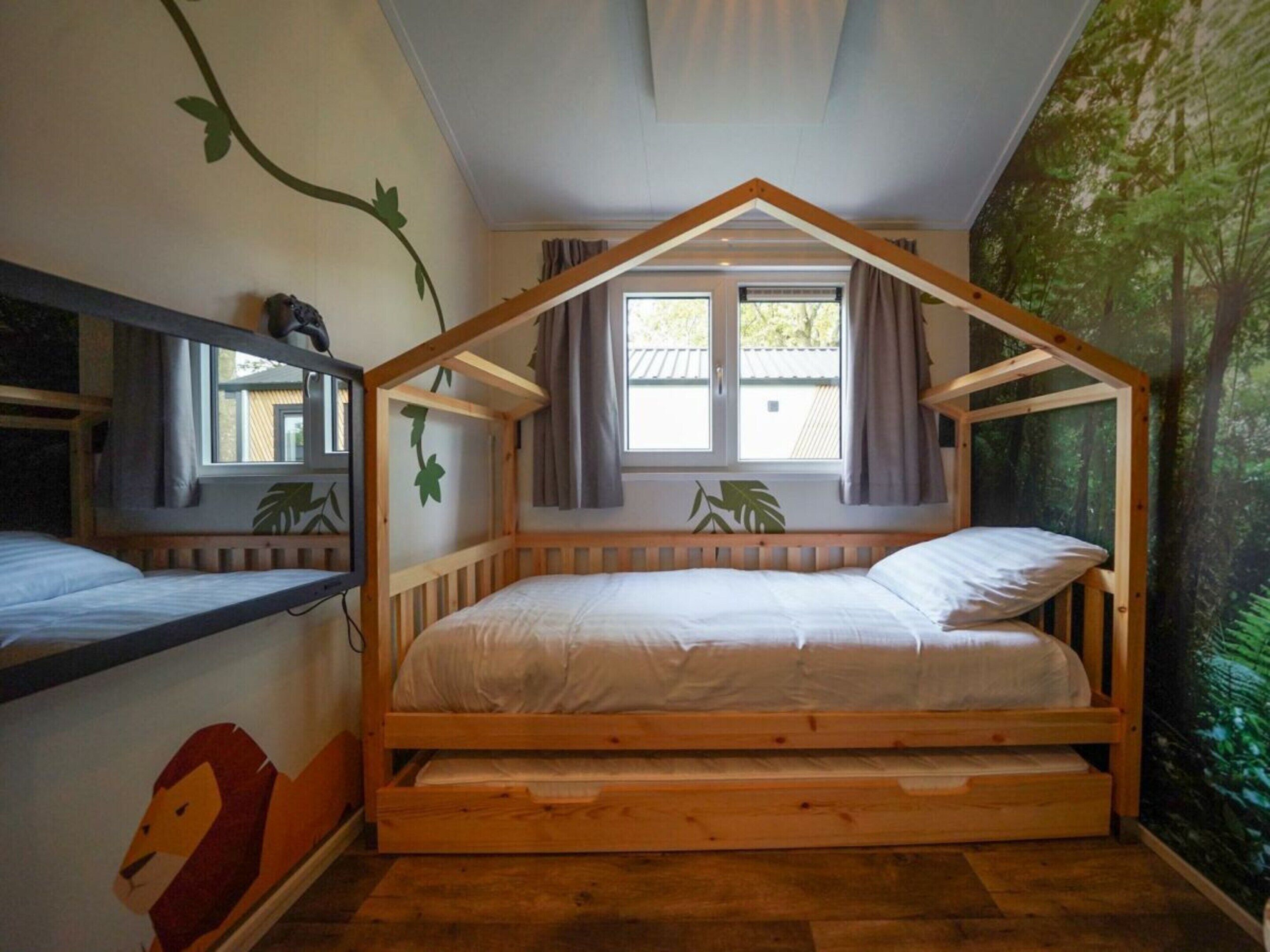 A wooden bunk bed with a sloped roof design, a window with curtains, and a forest-themed wall mural.