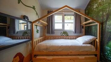 A wooden bunk bed with a sloped roof design, a window with curtains, and a forest-themed wall mural.