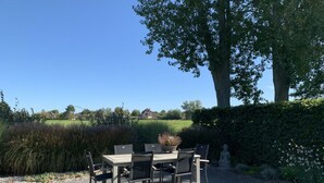 An outdoor patio with a table and chairs, surrounded by a hedge and a grassy area. - Restyled Koningshoeve 4 People (Schoorl)