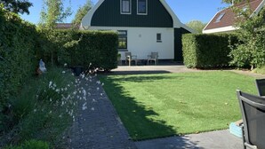 A barn with a white exterior and dark roof, surrounded by a well-maintained lawn and hedges. - Restyled Koningshoeve 4 People (Schoorl)