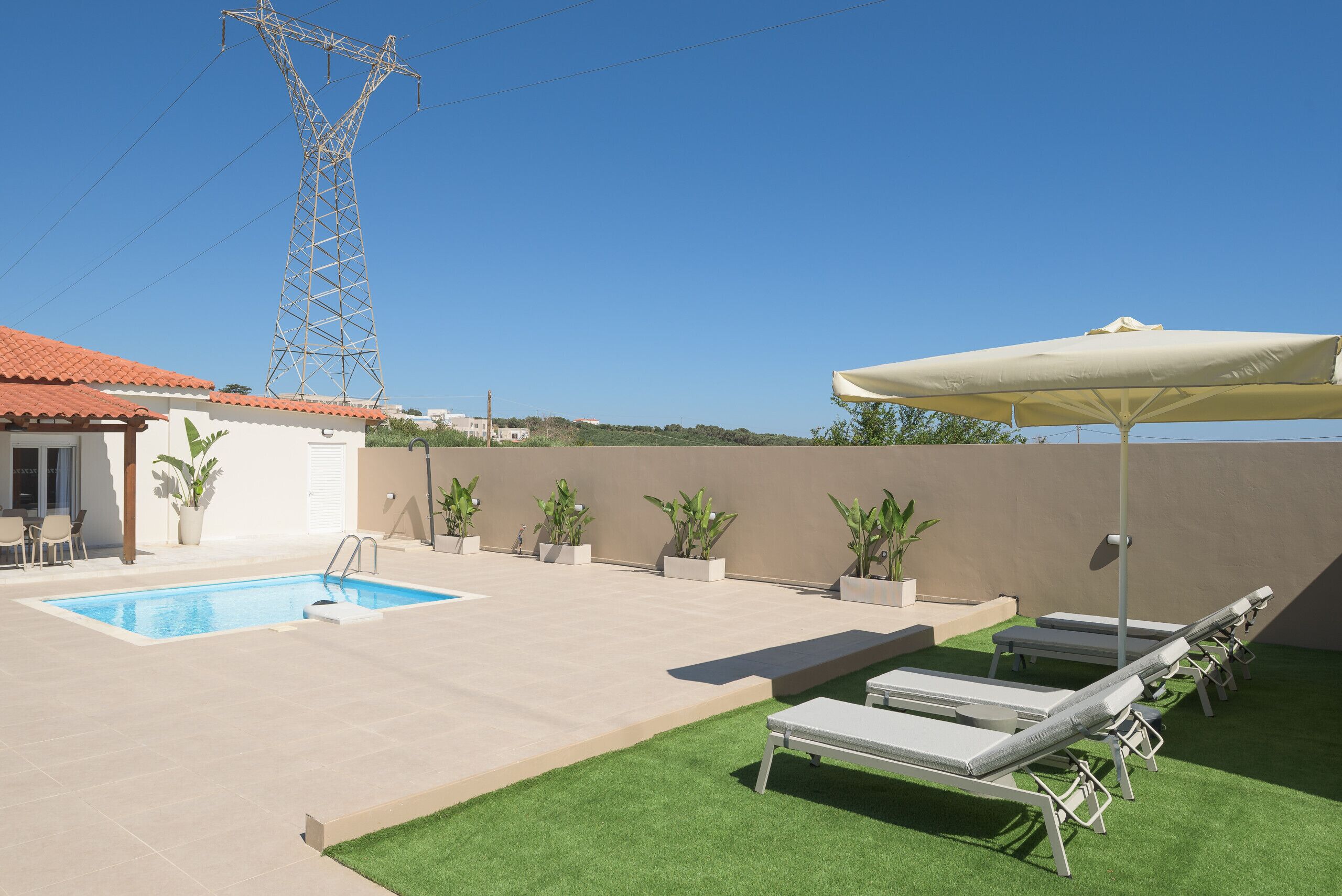 A swimming pool with lounge chairs and an umbrella, surrounded by potted plants and a building with a tiled roof.