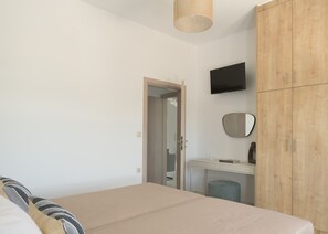Ein Schlafzimmer mit Bett, Kleiderschrank, Schreibtisch, Spiegel und Fernseher.