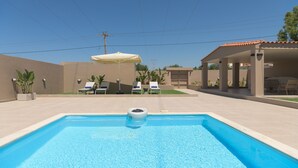 En swimmingpool med liggestole og en parasol, omgivet af en patio.