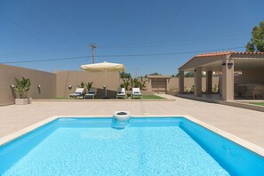 Ein Swimmingpool mit Liegestühlen und Sonnenschirm, umgeben von einer Terrasse.