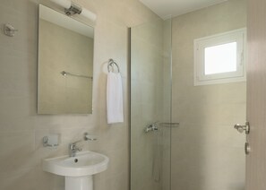 Ein Badezimmer mit einem weißen Waschbecken, einem Spiegel, einem Handtuchhalter, einer Glasdusche und einem kleinen Fenster.
