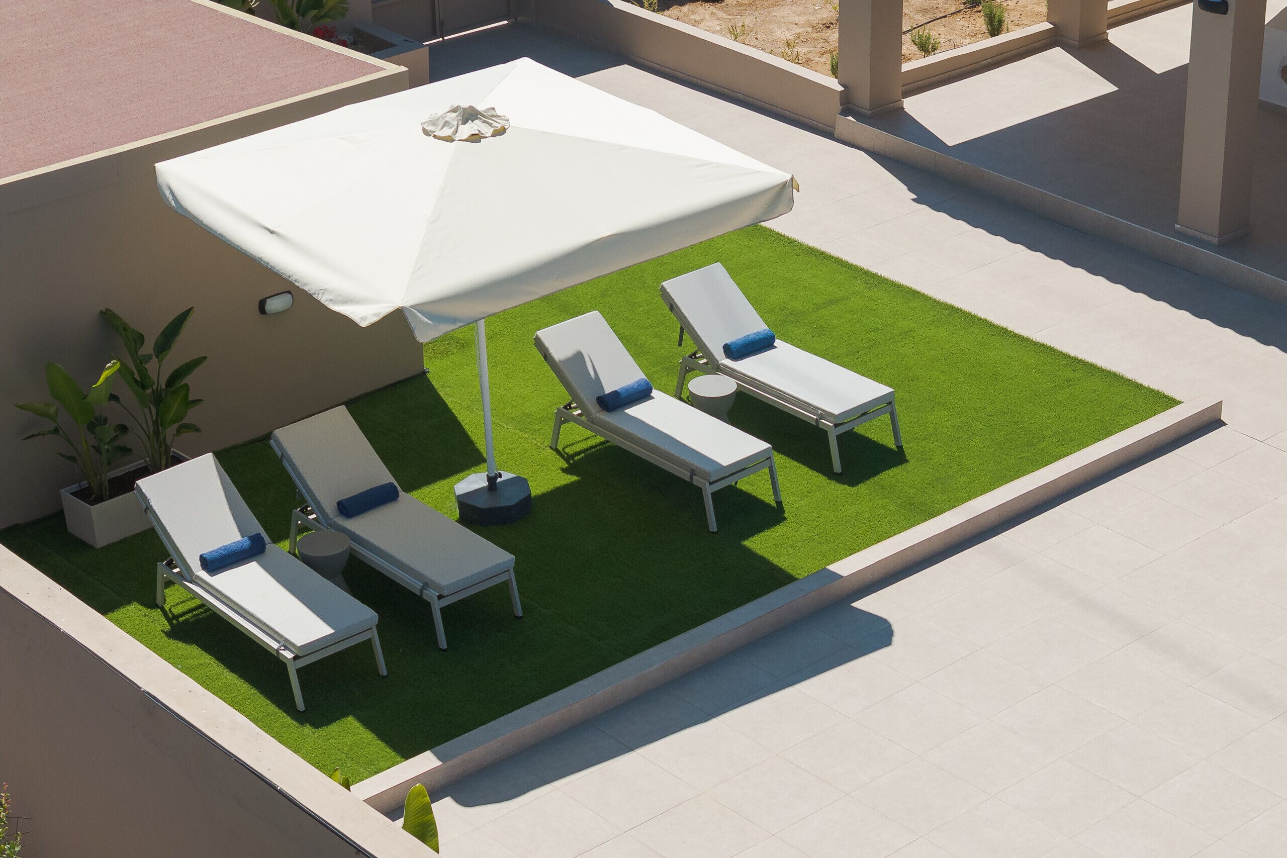 A rooftop patio with artificial grass, white lounge chairs, and a large umbrella.