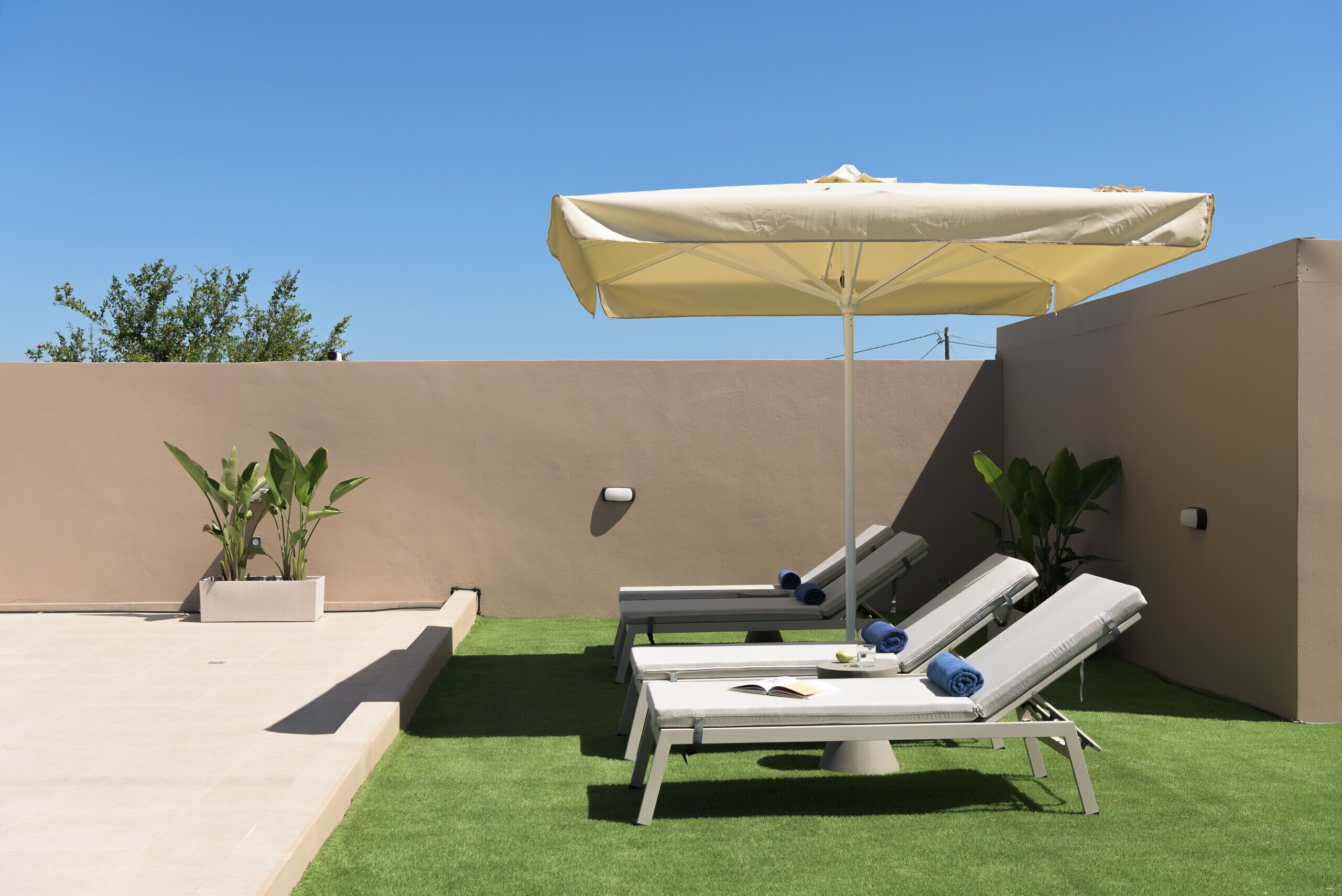 A rooftop lounge area with two sunbeds, a large umbrella, and potted plants.