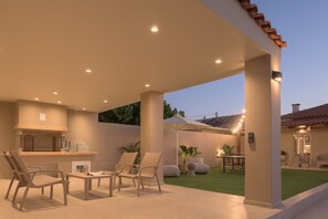 Eine Terrasse im Freien mit Grillplatz, Sitzgelegenheiten und guter Beleuchtung.