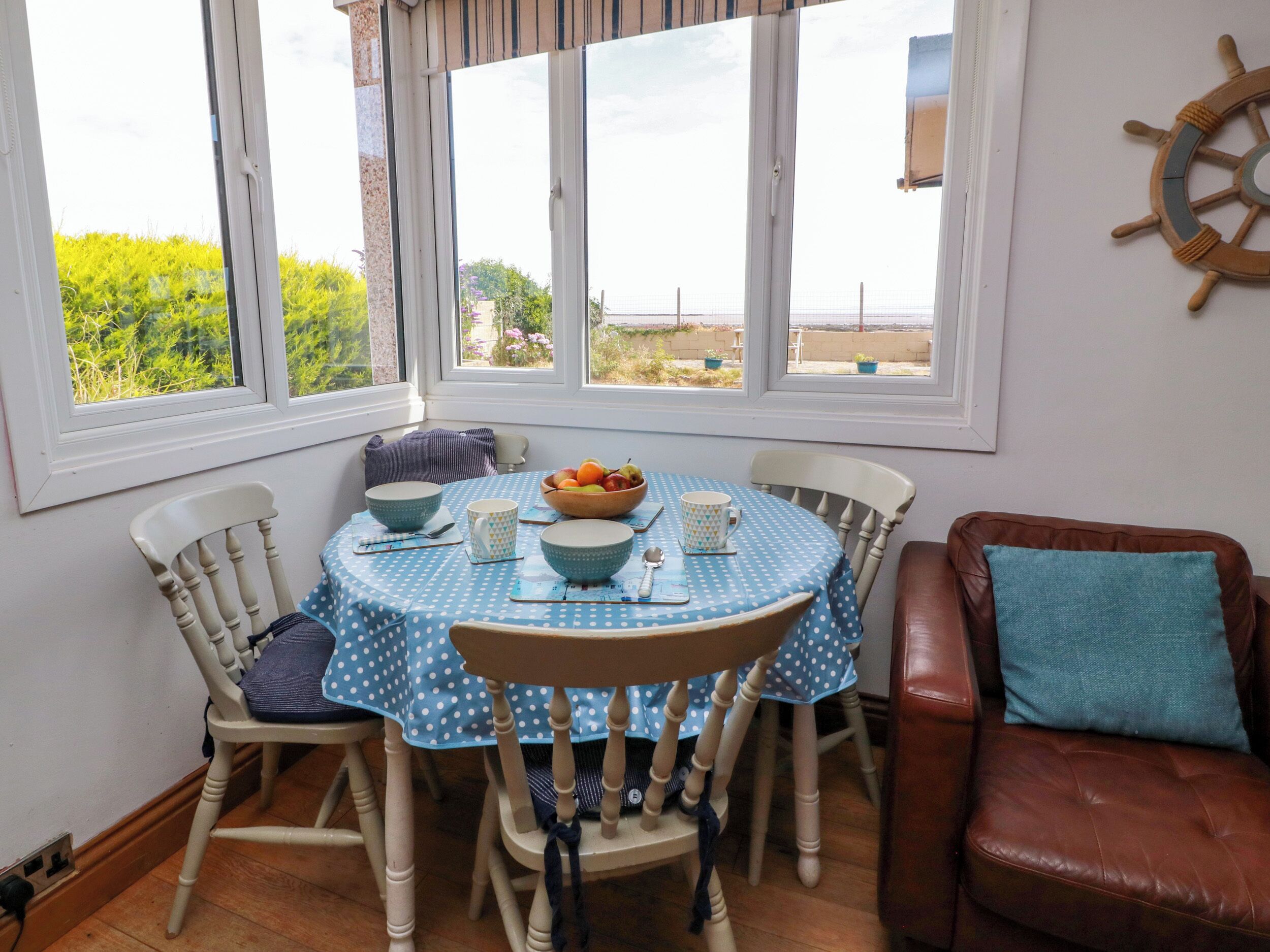 A dining area with a round table, chairs, and a view through large windows.