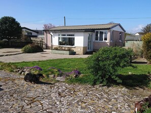 A two-story house with a front porch, a stone pathway, and a small garden with purple flowers.
