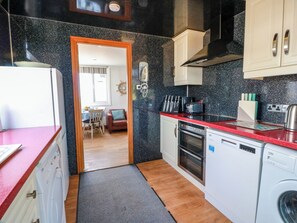 A compact kitchen with a washing machine, a coffee maker, and a toaster on the counter. - Wagtail Cottage (Dumfries)