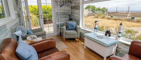 A room with a leather sofa, a grey armchair, a small table, and a view of the outdoors through large windows.