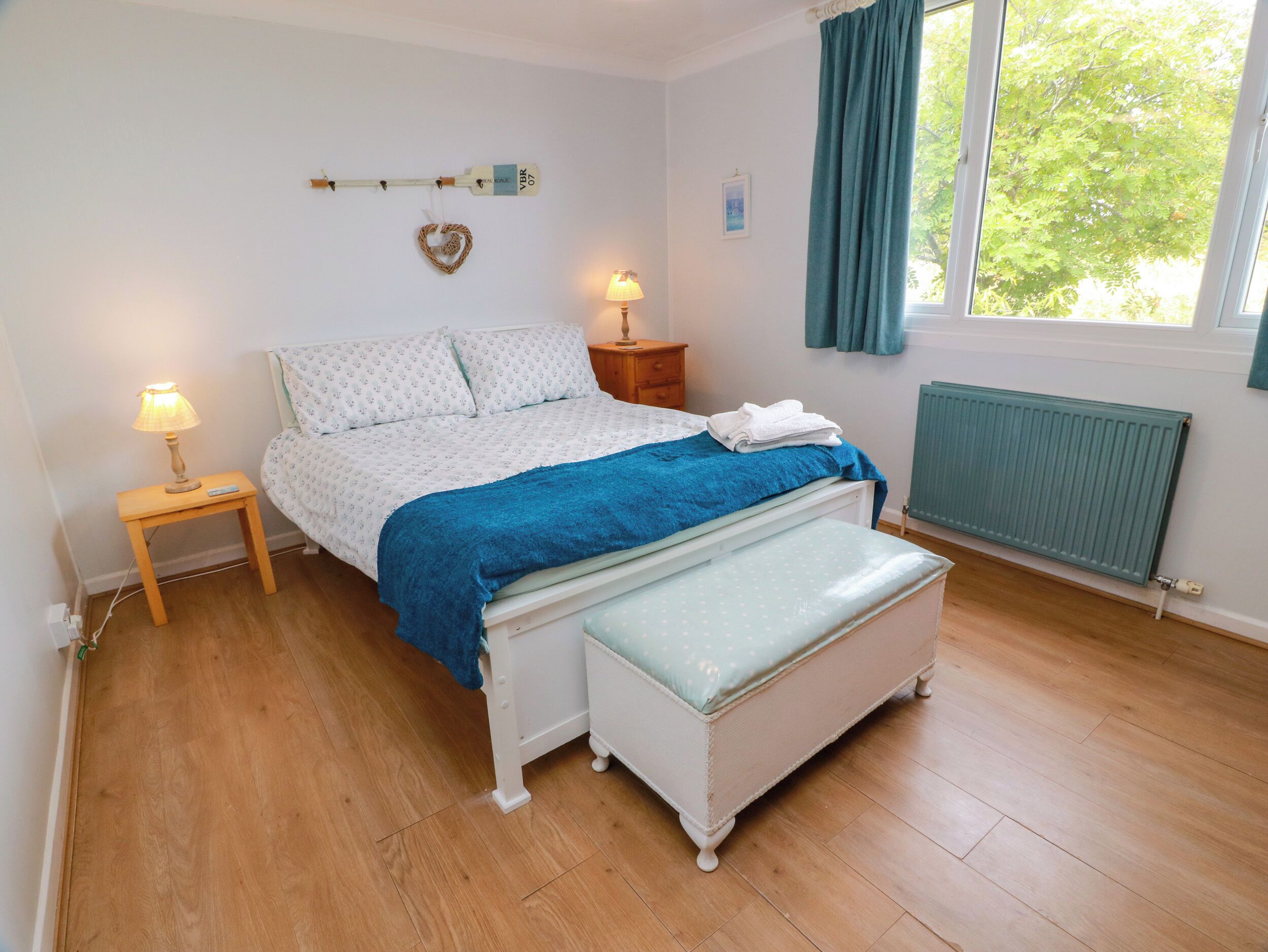 Een slaapkamer met een bed, nachtkastjes, een bankje, een radiator en een raam met gordijnen.