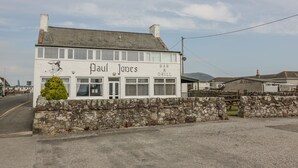 Um edifício de dois andares com a placa 'Paul Jones Bar & Grill', uma parede de pedra à frente e céu claro.