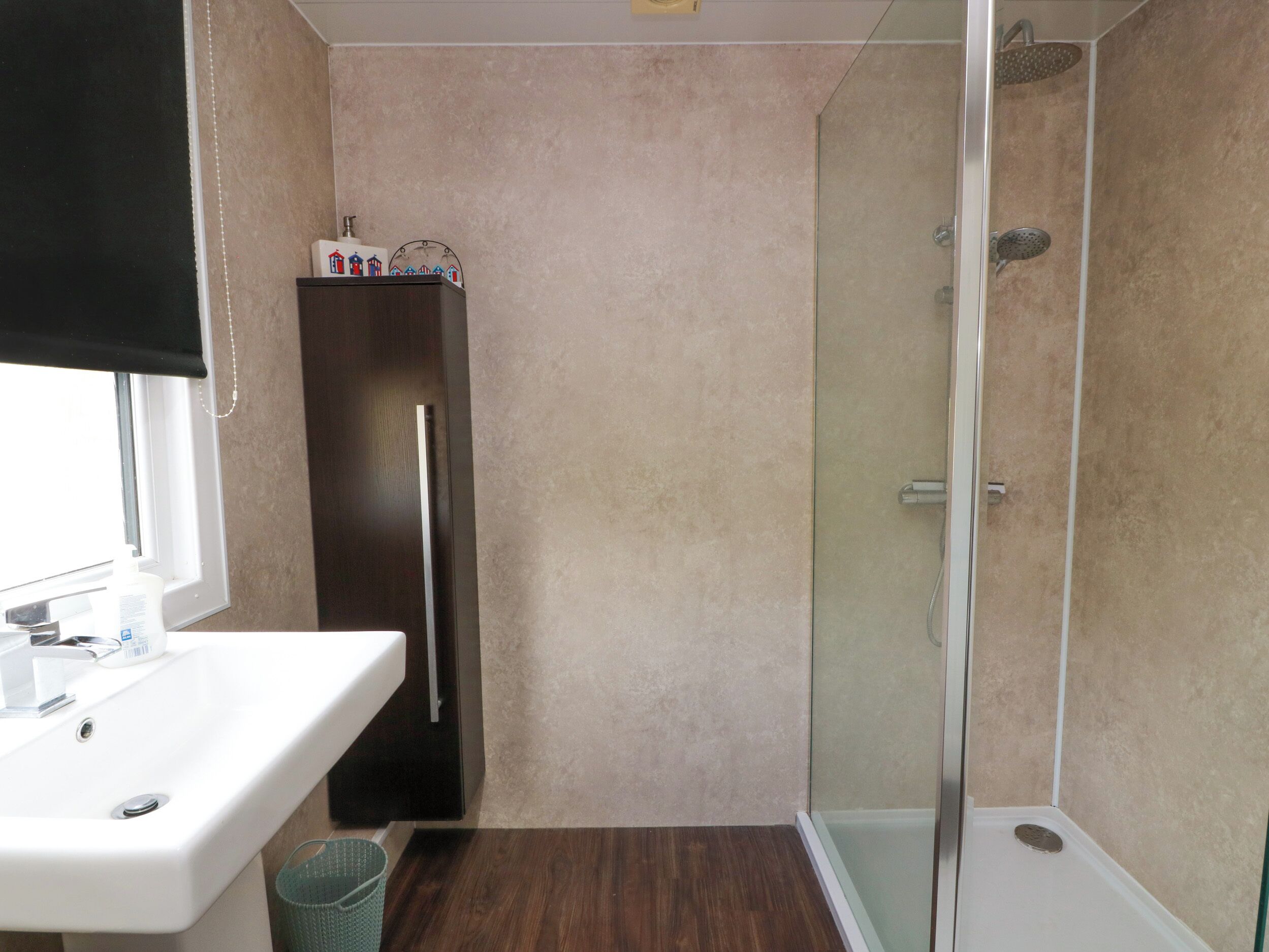 Un baño con un lavabo blanco, un mueble oscuro y una zona de ducha con cerramiento de vidrio.
