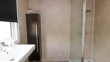 Un baño con un lavabo blanco, un mueble oscuro y una zona de ducha con cerramiento de vidrio.