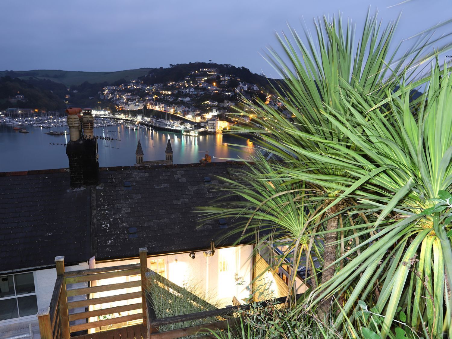 Un pueblo costero al atardecer con un puerto deportivo, una escalera de madera y una planta de palma.