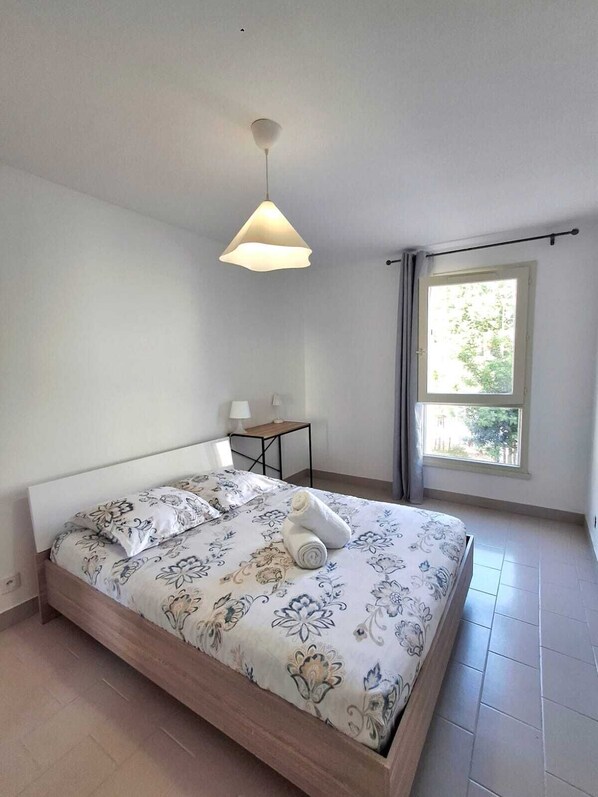 A bedroom with a bed, a bedside table, a lamp, a window, and a view of greenery outside. - Entire apartment with a breathtaking view of the Saint-Nazaire Cathedral. (Béziers)
