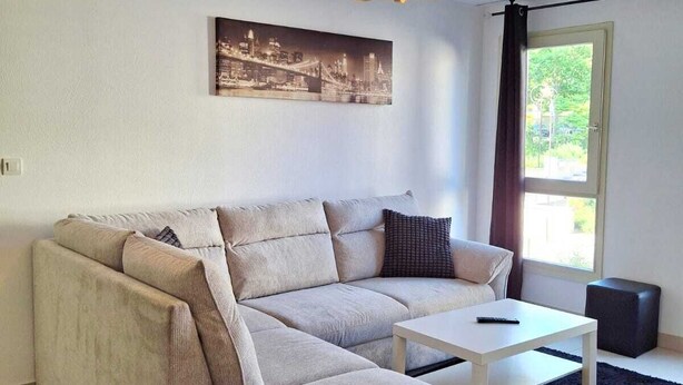 A modern living room with a sectional sofa, a white coffee table, and a cityscape picture on the wall. - Entire apartment with a breathtaking view of Saint Nazaire Cathedral. (Béziers)