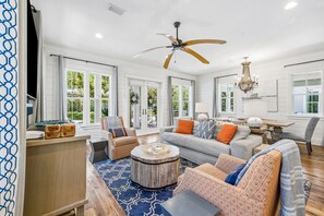 A spacious living room with a ceiling fan, a chandelier, and a large window providing a view of greenery outside. - WaterColor Escape with Pool and Screened-in Porch (Santa Rosa Beach)