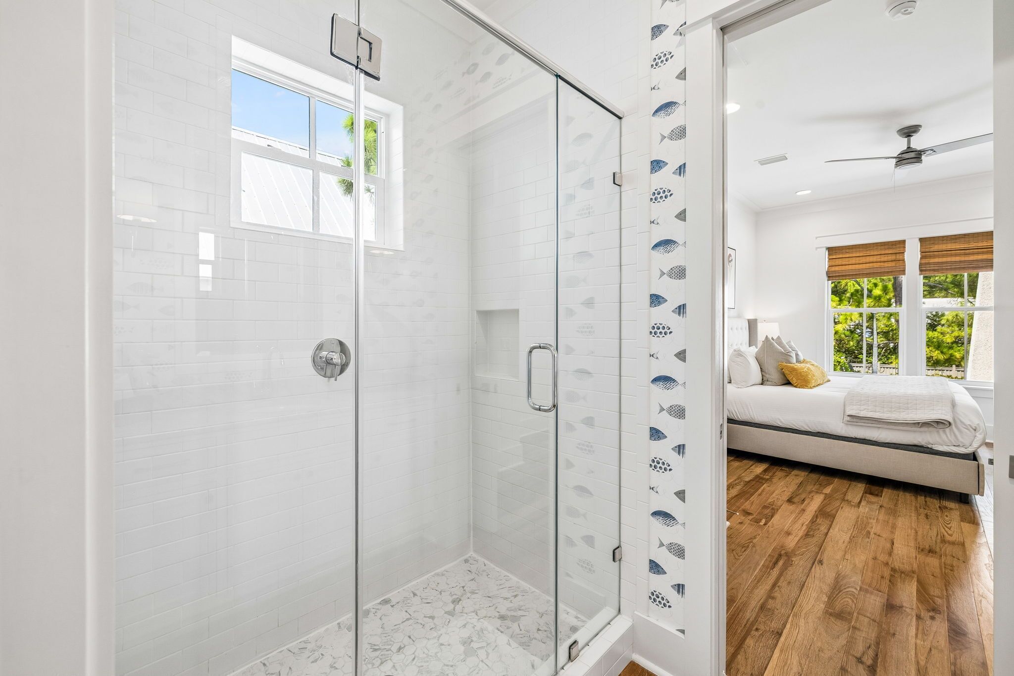 A modern bathroom with a glass shower enclosure, white tiled walls, and a visible window.