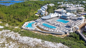 Eine Vogelperspektive zeigt einen luxuriösen Urlaubsort mit mehreren Schwimmbecken, einem großen Gebäudekomplex und bewaldeter Umgebung.