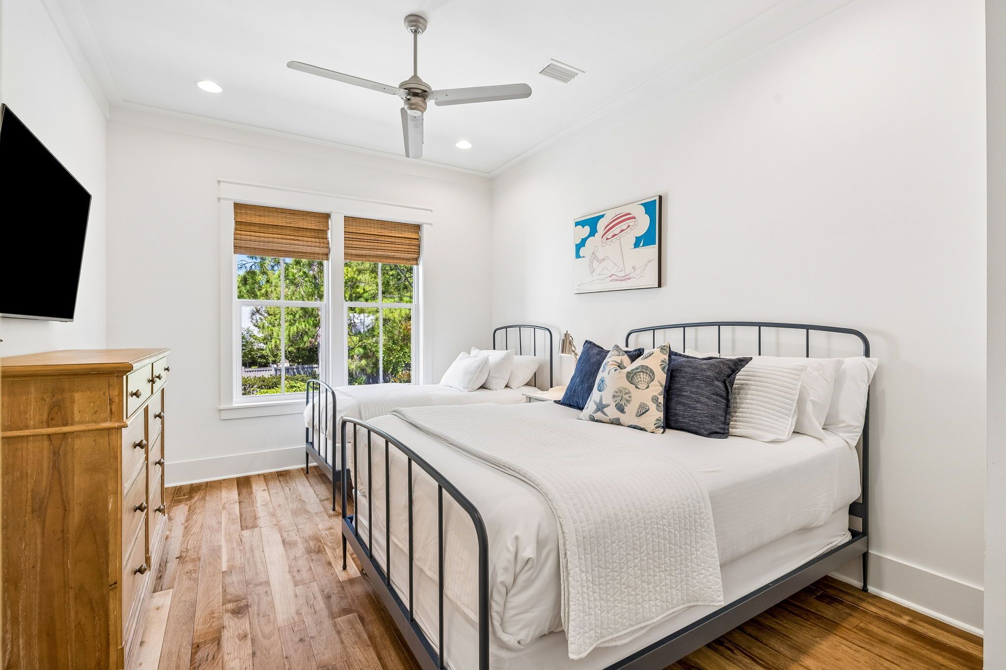 Une chambre à coucher avec un lit, une commode en bois, un ventilateur de plafond et une fenêtre avec des stores.