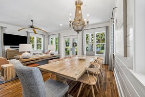 A spacious dining area with a large wooden table and multiple chairs, a chandelier, and a television mounted on the wall. - WaterColor Escape with Pool and Screened-in Porch (Santa Rosa Beach)
