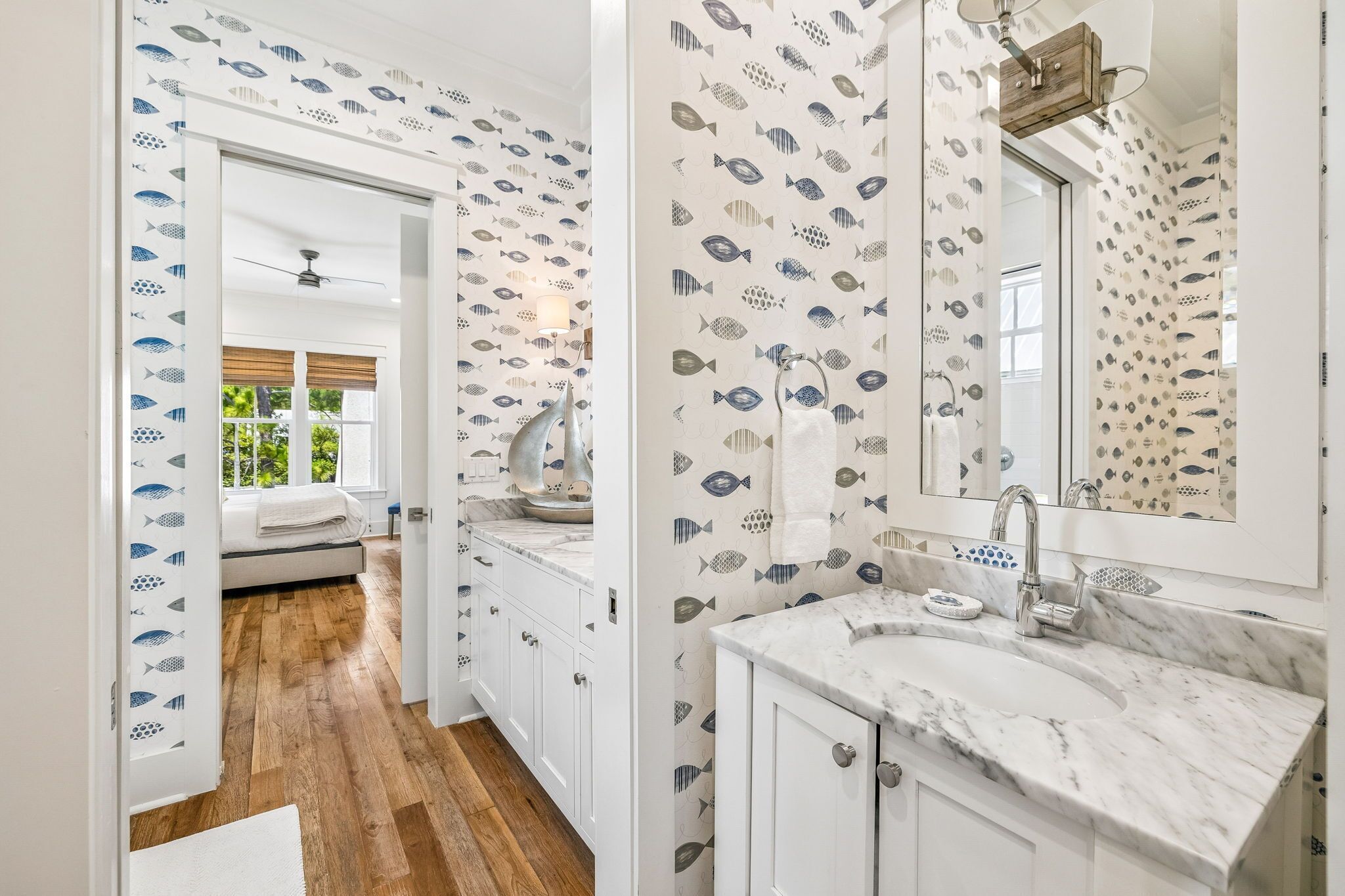 A modern bathroom with a large mirror, a marble countertop, and a fish-patterned wallpaper.