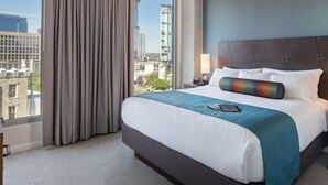 Ein Hotelzimmer mit einem großen Bett, Blick auf die Stadt und einem mit Vorhängen versehenen Fenster.