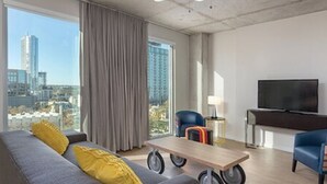Ein modernes Hotelzimmer mit einer Couch, einem kleinen Tisch, einem Fernseher und Blick auf die Stadt.