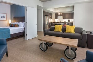 Ein modernes Hotelzimmer mit Bett, Sofa, kleinem Tisch und einer Küchenzeile im Hintergrund.