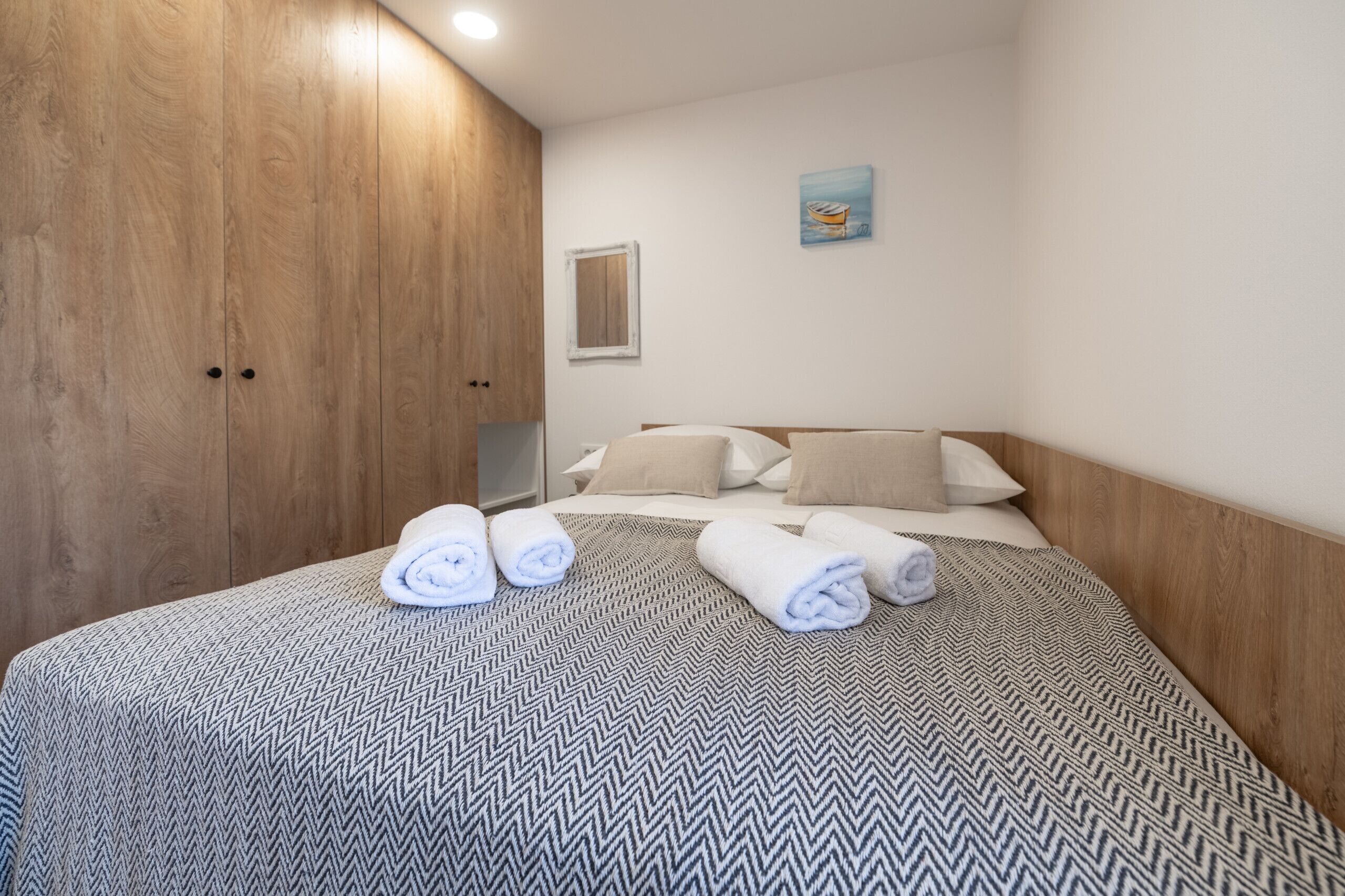A hotel room with a bed, wooden wardrobe, and a painting on the wall.