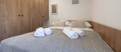 A hotel room with a bed, wooden wardrobe, and a painting on the wall.