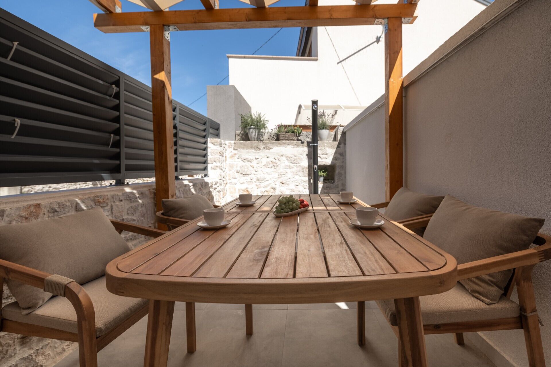 Een houten tafel met stoelen buiten, een stenen muur en een pergola.