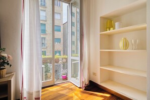 A room with a sliding glass door leading to a balcony, a wooden floor, and a white shelving unit with decorative items. - Garibaldi 44 - Milan Most Vibrant District (Milano)