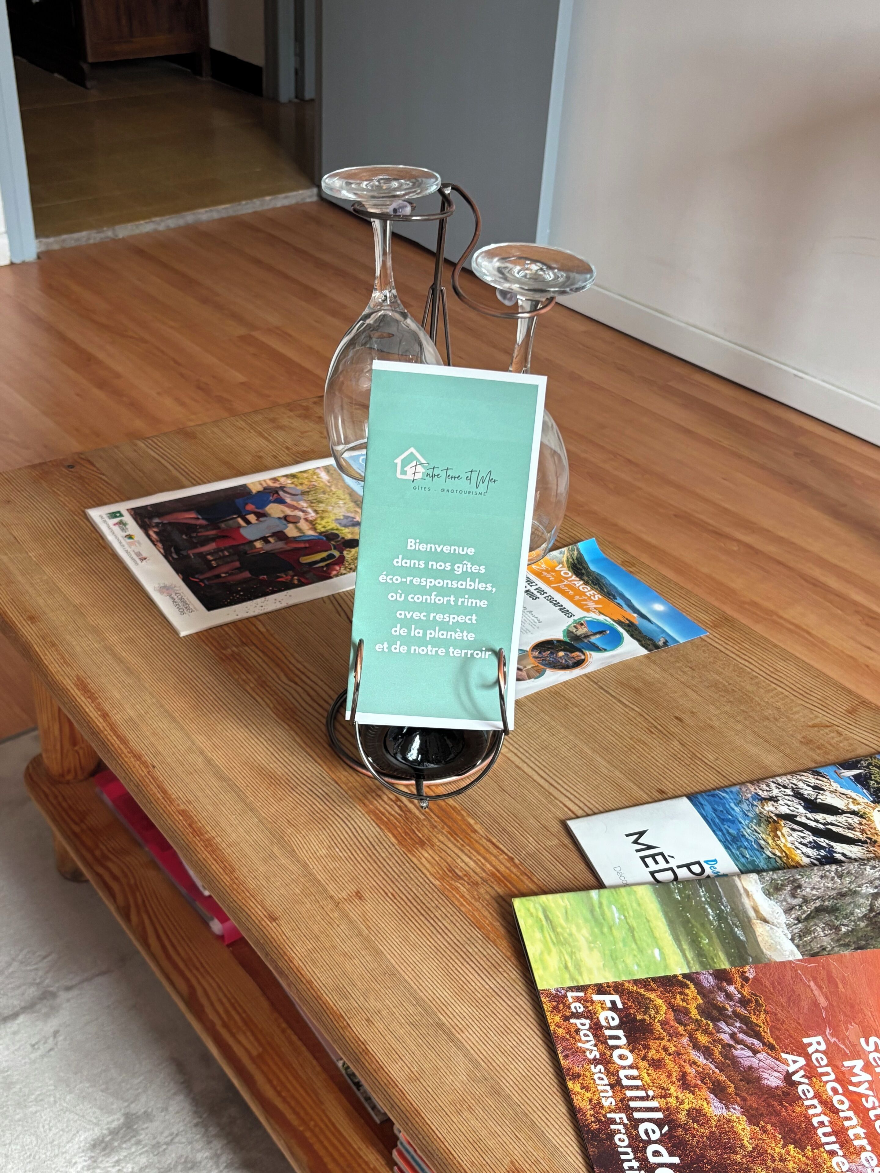 A wooden table with a welcome sign, brochures, and two glass candle holders.