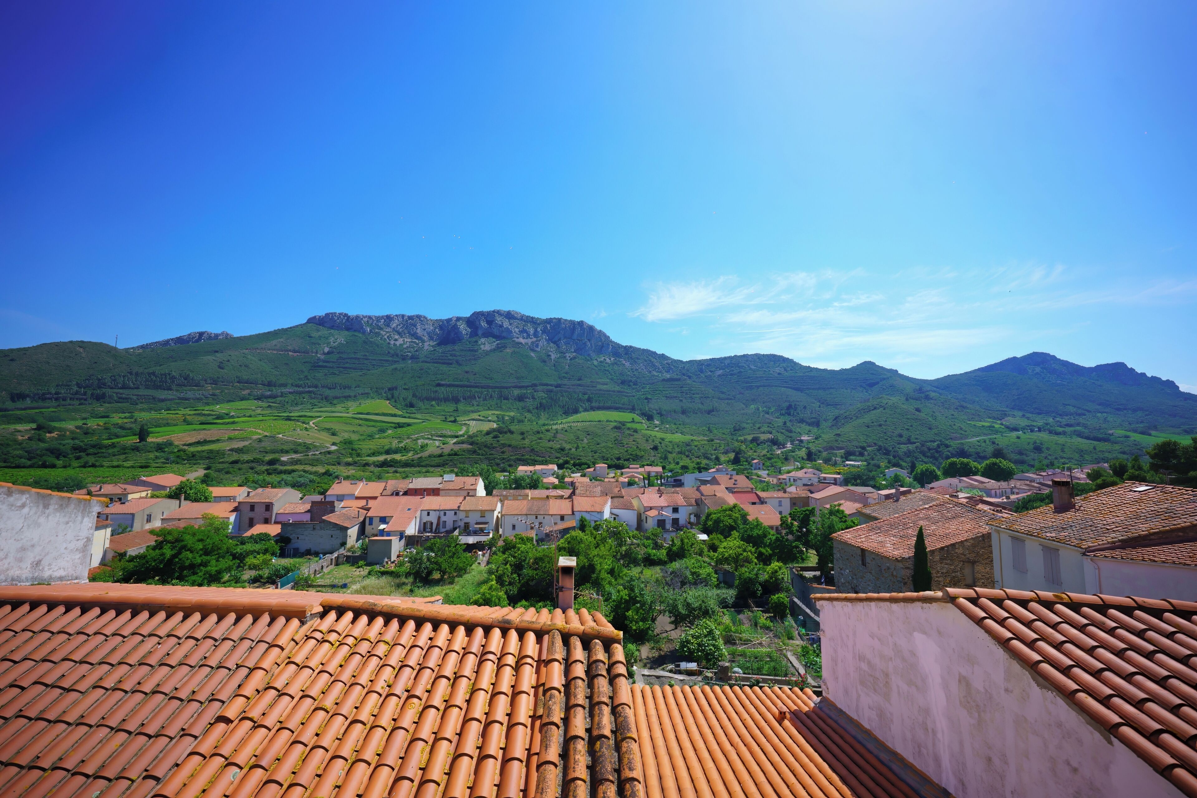 Un villaggio con edifici a tetto di tegole, una montagna sullo sfondo e un cielo sereno.