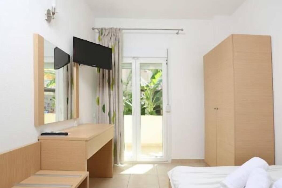 Un dormitorio con cama, escritorio, televisor y puerta corrediza a un balcón.