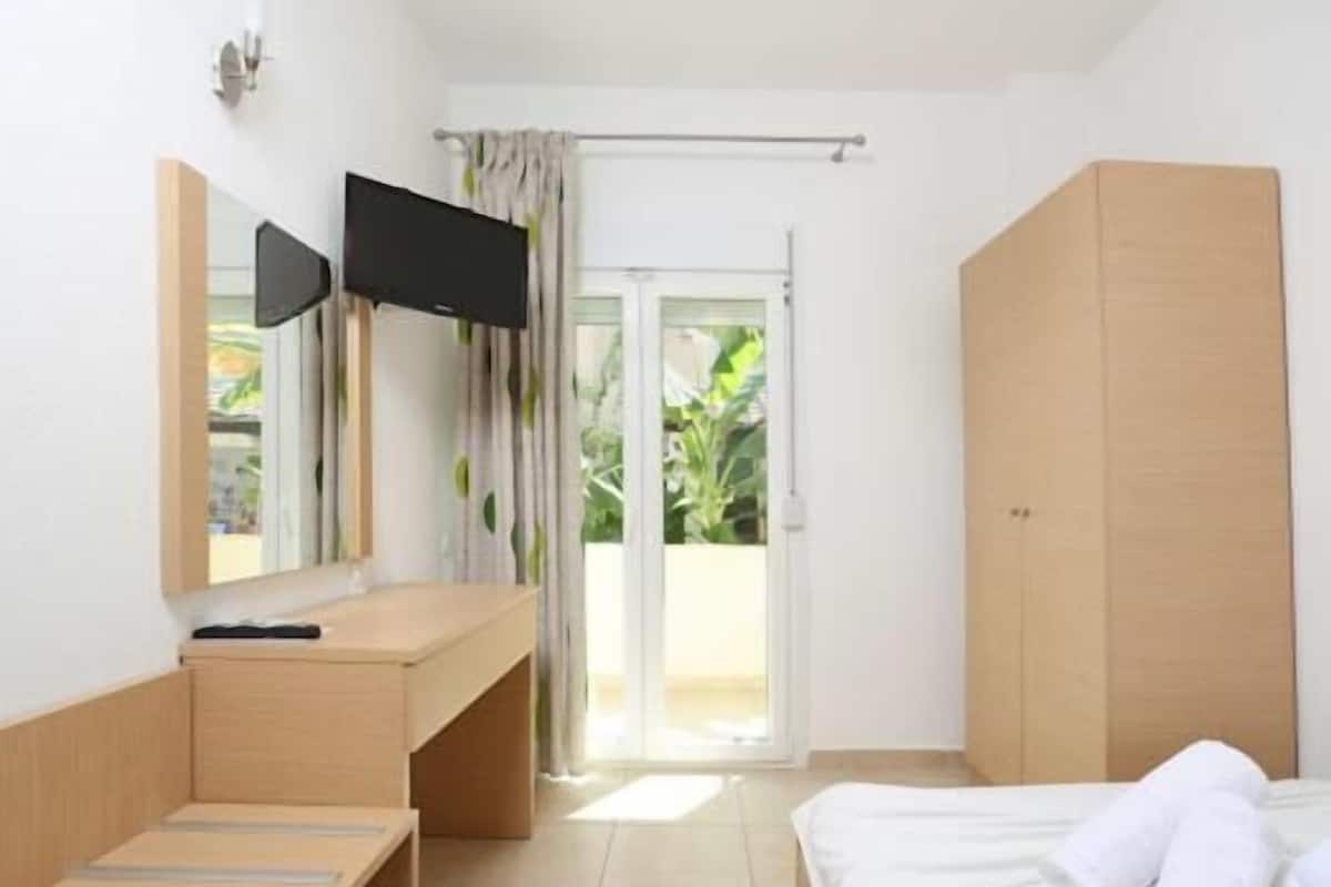 Un dormitorio con cama, escritorio, televisor y puerta corrediza a un balcón.