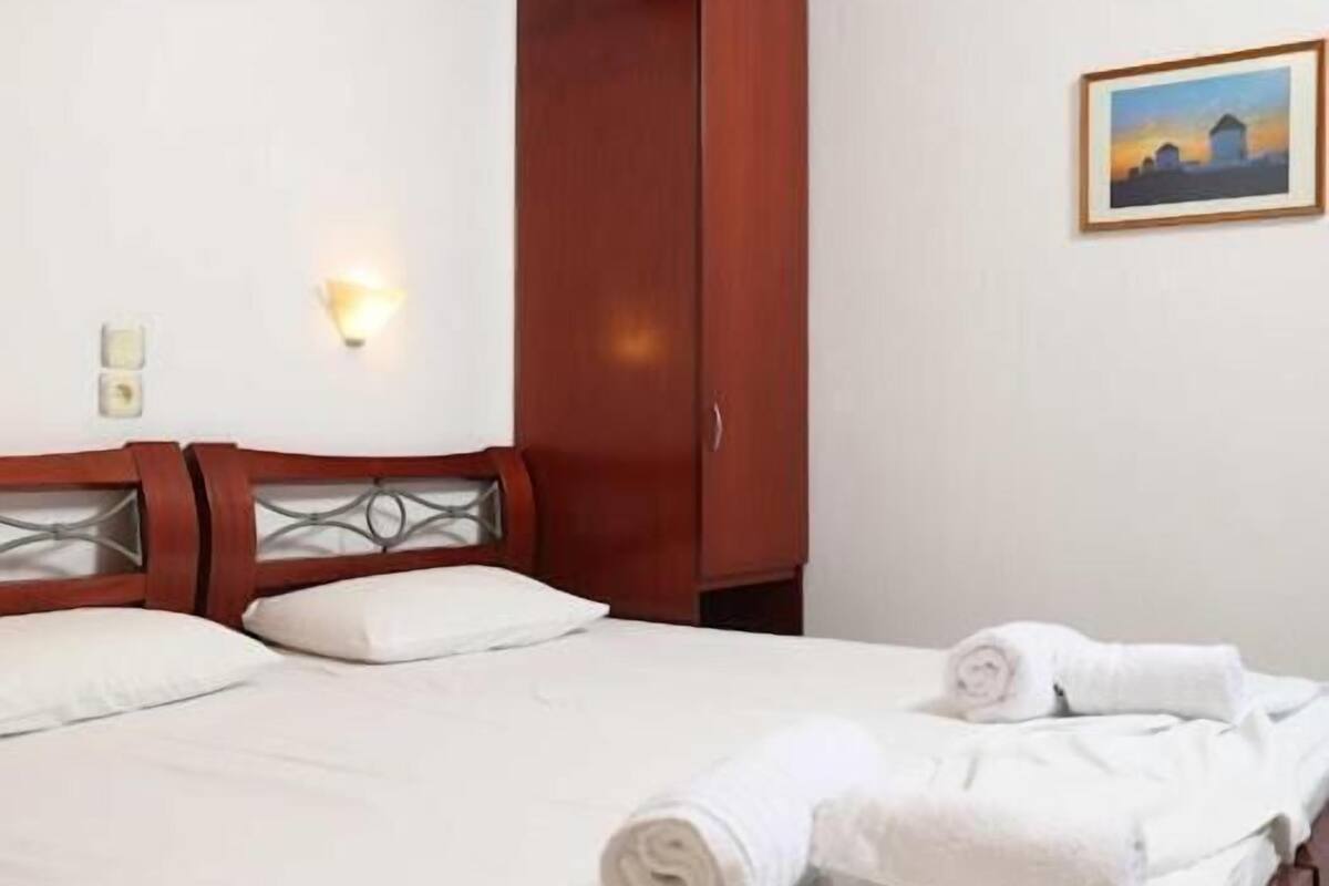 Habitación de hotel con cama, armario de madera, luz empotrada en la pared y un cuadro enmarcado.