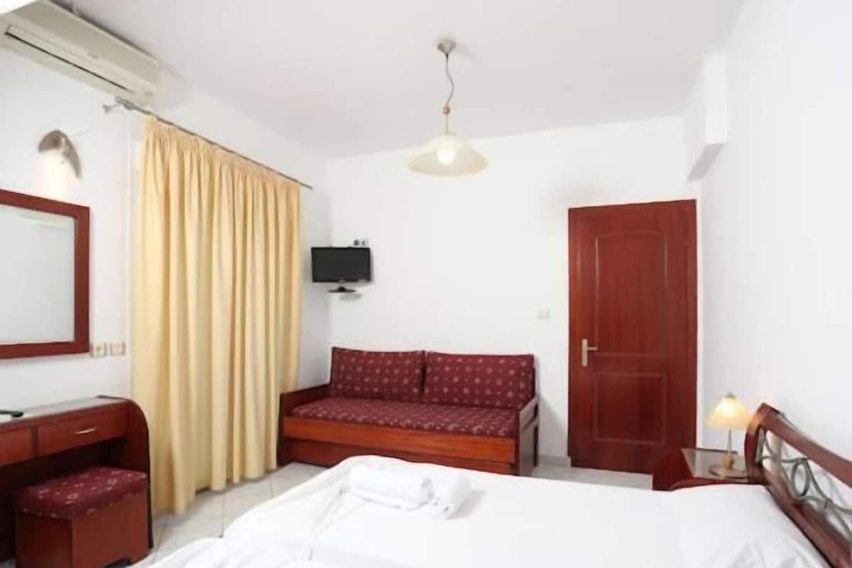 Habitación de hotel con cama, escritorio, sillón, sofá, televisión y armario.